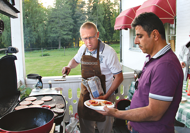 Nisse Graan (KD), kvällens grillmästare, serverar Thaer Tomeh en nygrillad hamburgare.
